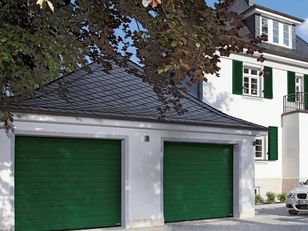 Doppelgarage mit zwei moosgrünen Sektionaltoren an einem weiß verputzten Haus