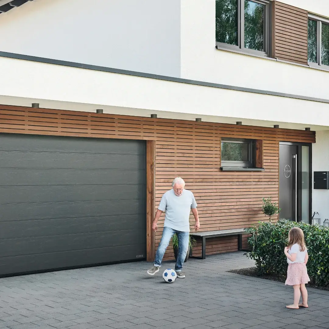 Vater und Tochter spielen Fußball vor der geöffneten Garage ihres Hauses