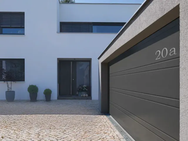 Gepflasterte Hofeinfahrt zu einer Garage mit grauem Sektionaltor