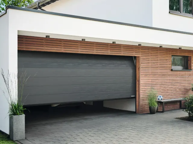 Anthrazitfarbenes Sektionaltor neben einer Fassade aus senkrechten Holzlatten