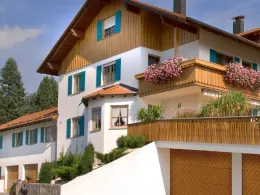 Landhaus mit Balkon und Blumenkästen, daneben eine Garage mit Holzoptik-Tor