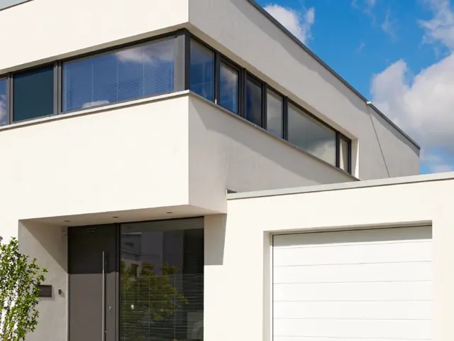 Weißer Neubau mit großem hellem Garagentor unter einem Vordach