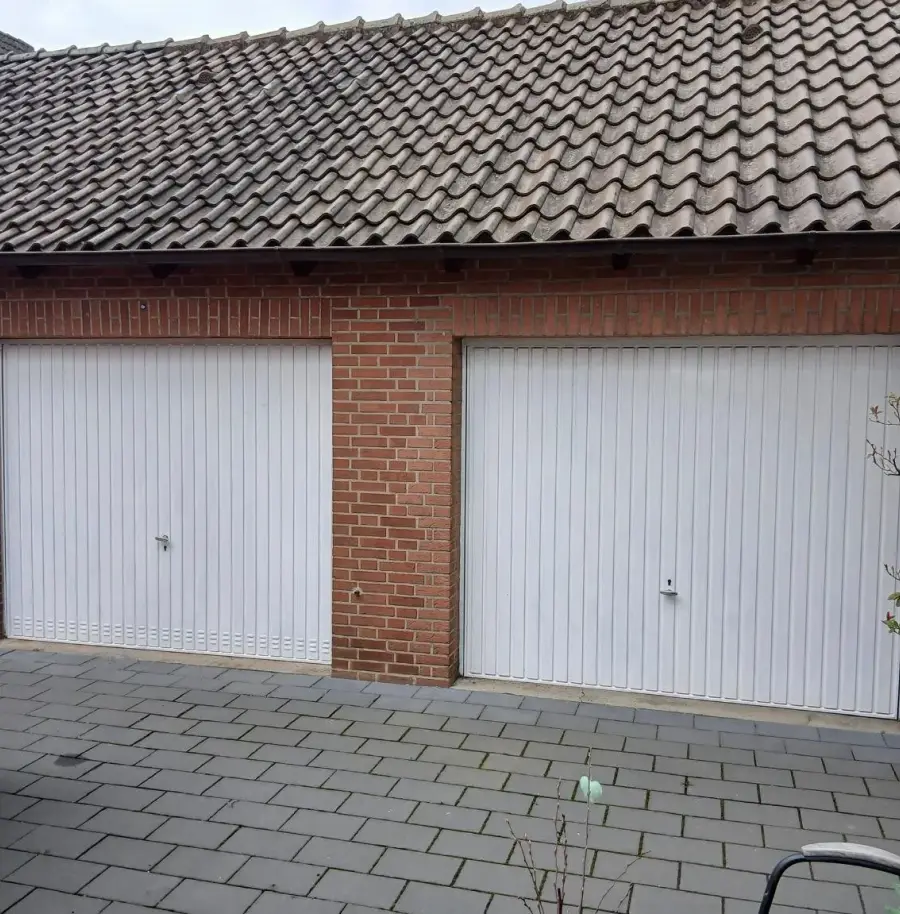 Doppelgarage aus rotem Klinker mit zwei weißen Schwingtoren