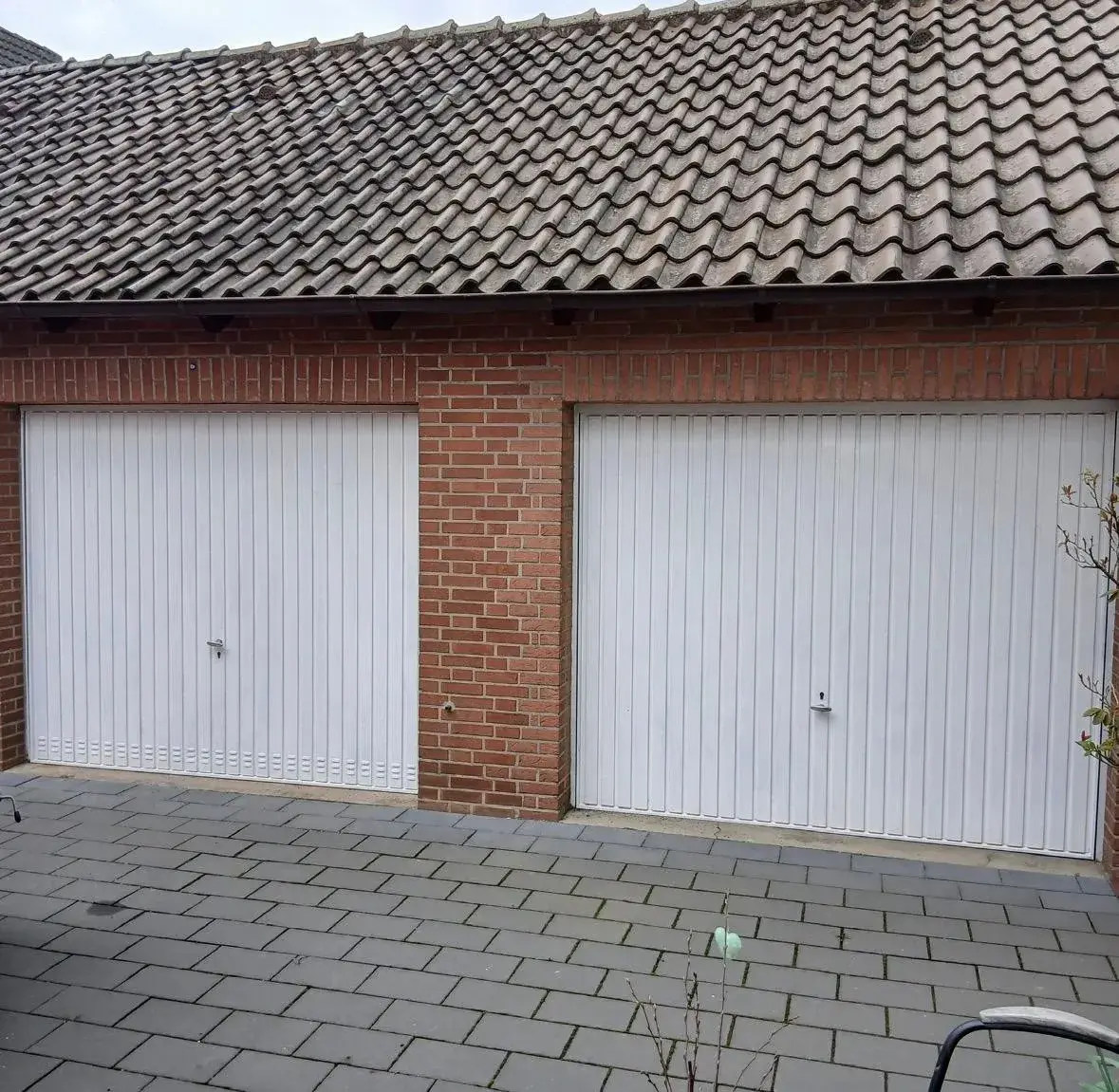 Doppelgarage aus rotem Klinker mit zwei weißen Schwingtoren